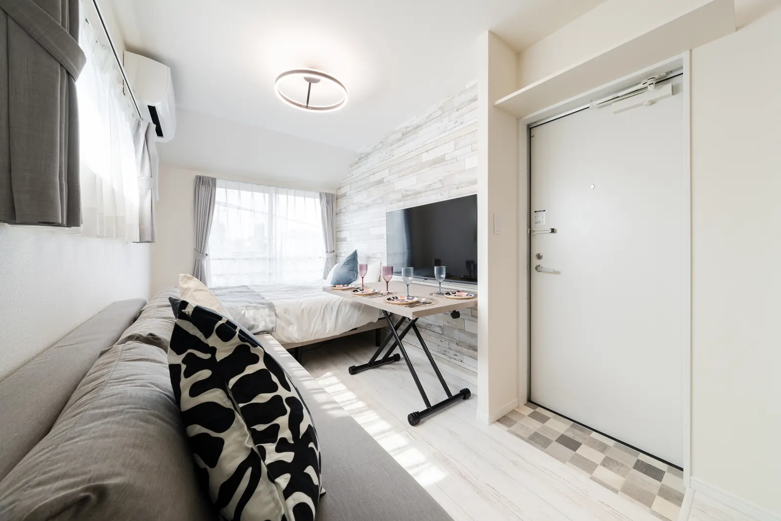 Studio unit at Intervia Horikiri with grey sofa bed, dining table, wall-mounted TV and double bed by the window